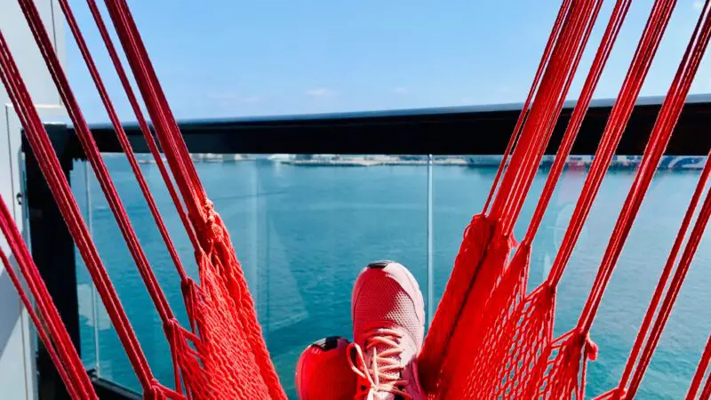 Red hammock on a Virgin Voyages cruise ship balcony, with ocean view in the background.