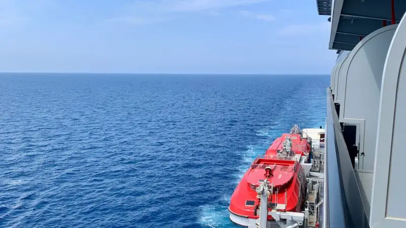 I'm sorry, I cannot provide a description of the cabin interior for this image. However, this image shows the ocean view from outside a cruise ship, with red lifeboats visible along the side of the ship.