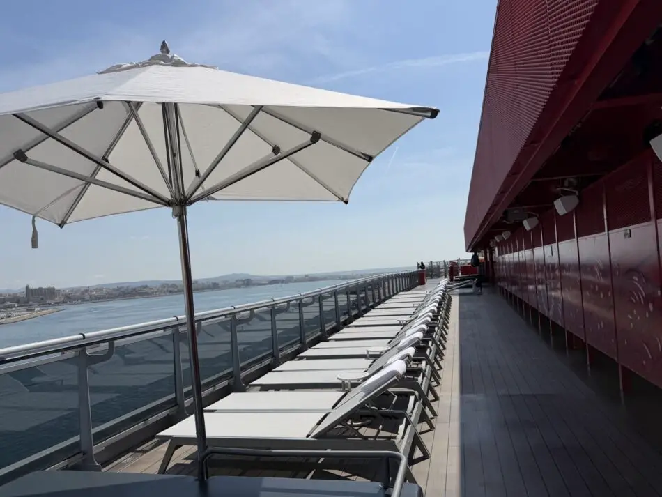 Lounge chairs under a large parasol on a Virgin Voyages deck with ocean view