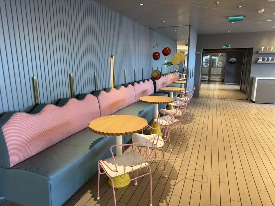 Pastel lounge with pink and teal upholstery, round wooden tables, and pink metal chairs