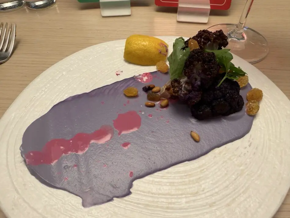 Gourmet plated dish with purple sauce, charred cauliflower, lemon, greens