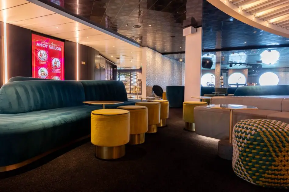 Stylish Virgin Voyages cruise ship lounge with teal sofas and yellow ottomans