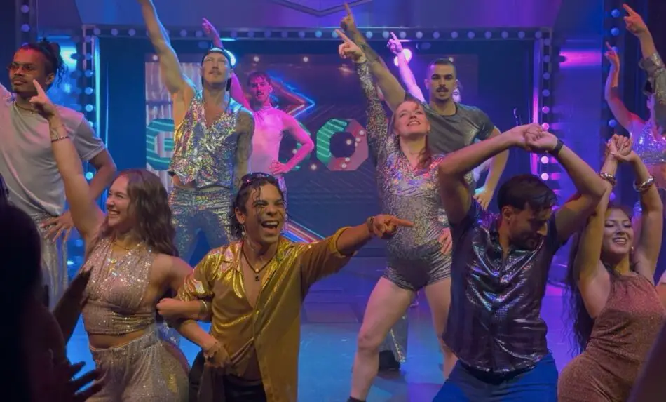 Dancers in glittery outfits perform on a brightly lit stage