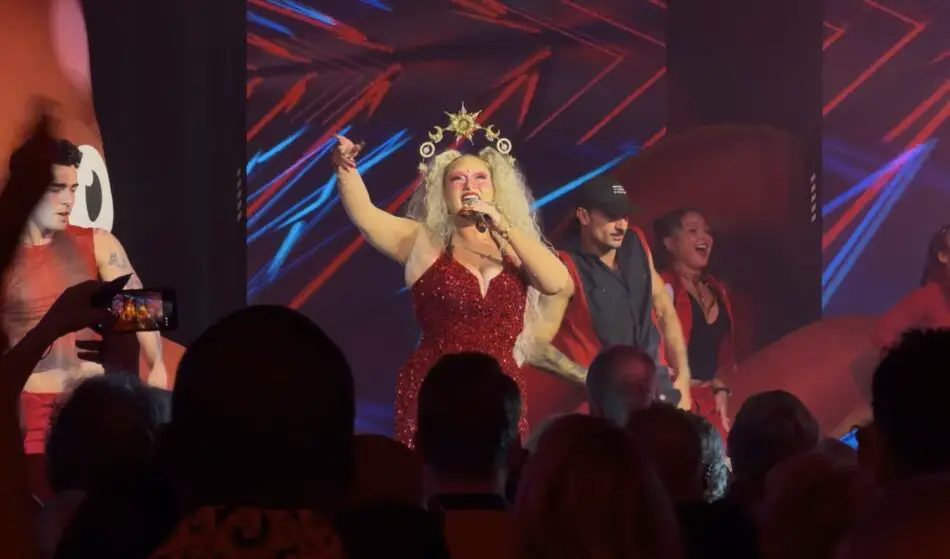 Lead singer in a red sequined dress with crown performs on stage with backup dancers