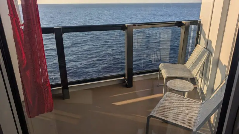 Balcony view from a Virgin Voyages cruise ship cabin, featuring two chairs and a small table overlooking the ocean.
