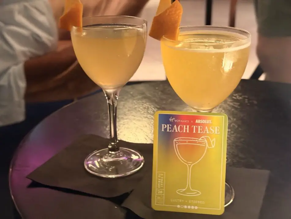 Two peach cocktails on a table with a Peach Tease card on a Virgin Voyages cruise ship