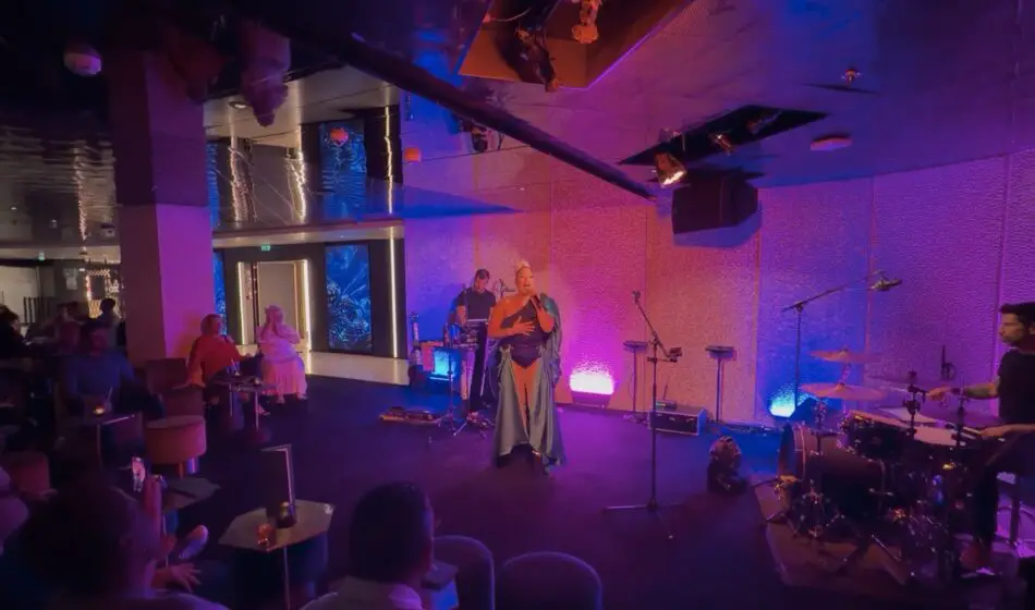 Live singer in a blue gown performs on stage with a drummer as the audience watches