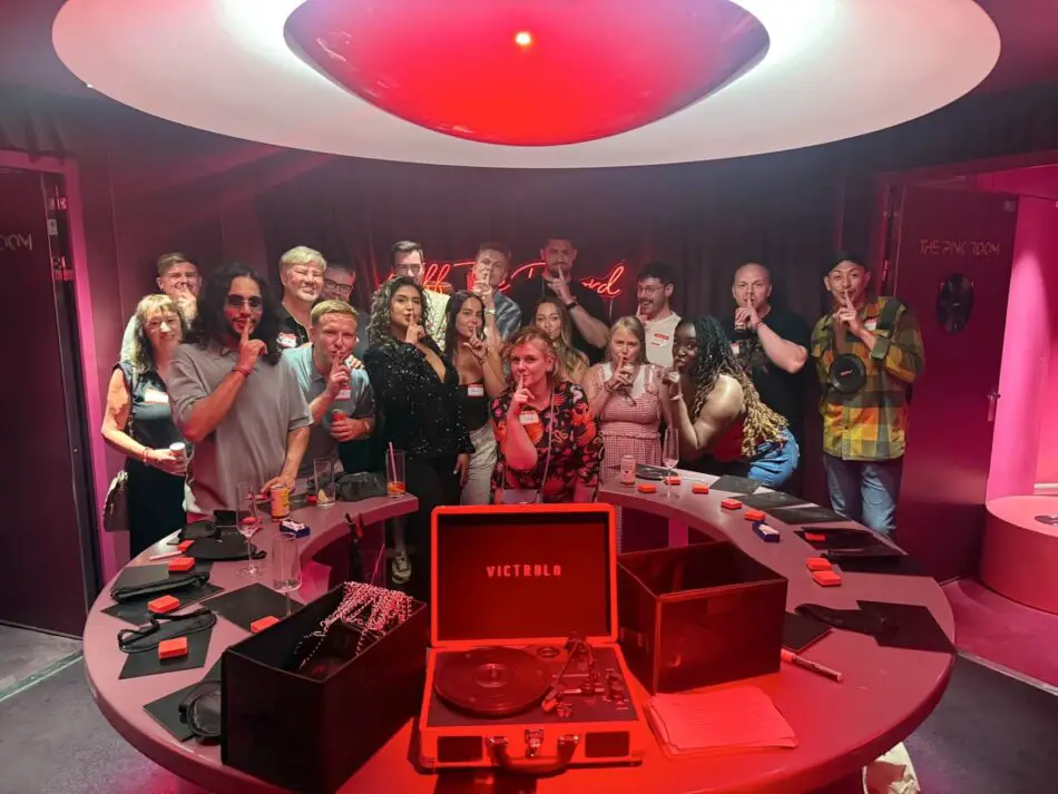 Group of guests posing in a red-lit Virgin Voyages cruise ship club