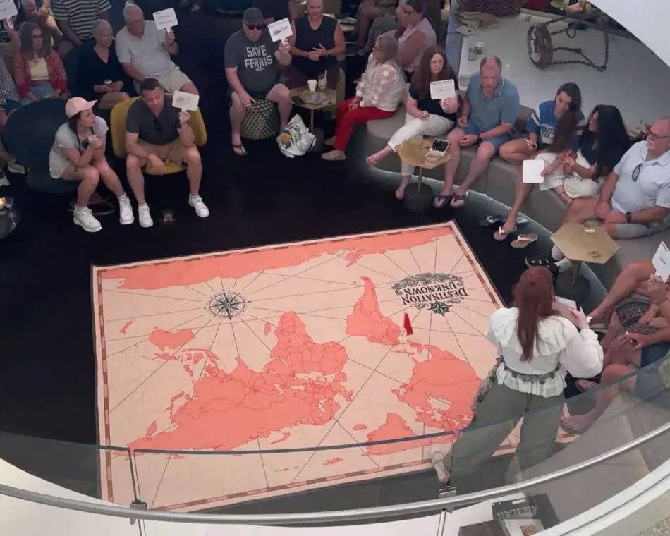 Group of passengers seated around a large pink world map on a Virgin Voyages cruise ship