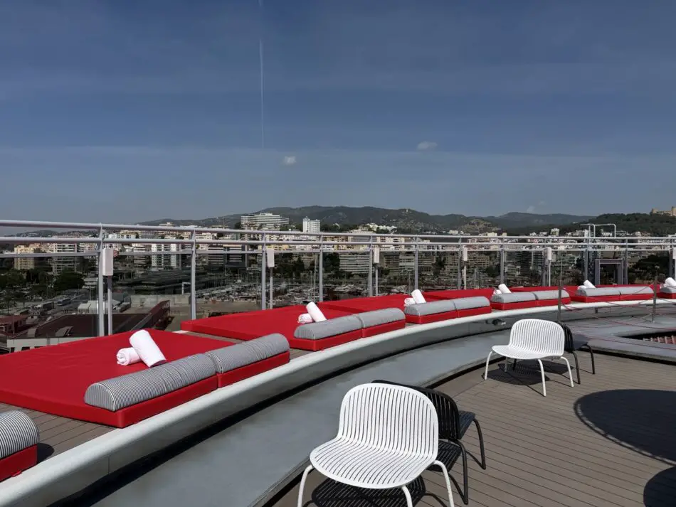 Rooftop cruise deck with red cushioned loungers and white chairs overlooking a cityscape