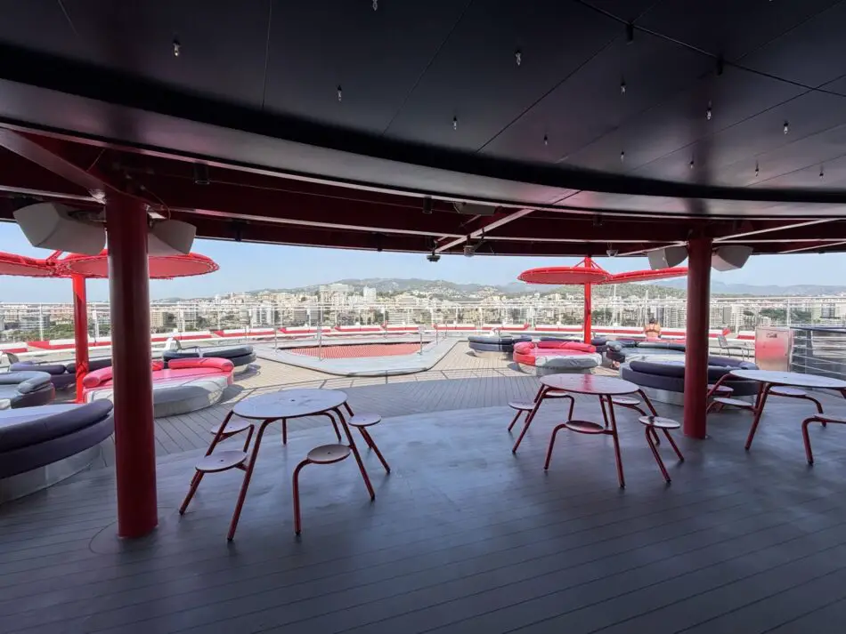 Outdoor lounge deck on a Virgin Voyages cruise ship with red seating