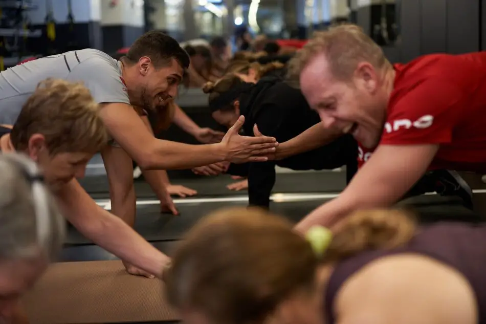 Group of people in a gym class leaning forward to high-five on exercise mats