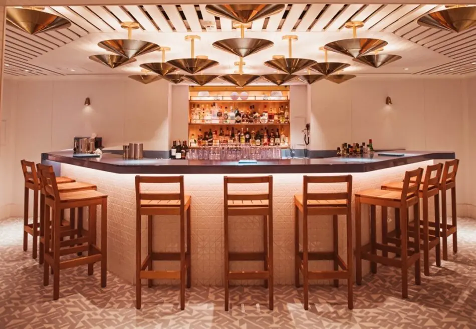 Bar on a Virgin Voyages cruise ship with backlit liquor shelves and wooden stools
