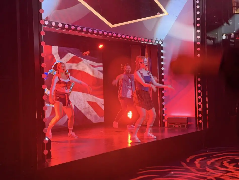 Dancers perform on a red-lit stage with a geometric backdrop and bulb-lined frame