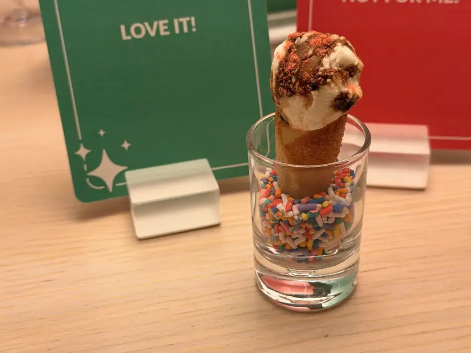 Ice cream cone standing in a glass filled with colorful sprinkles on a wooden table