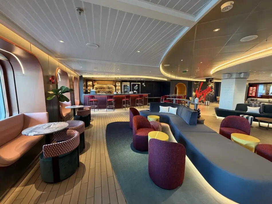 Lounge area on a Virgin Voyages cruise ship with colorful seating and a bar