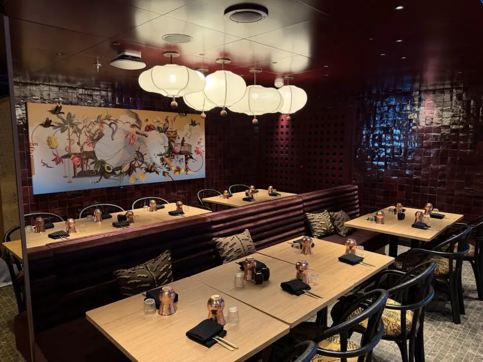 Restaurant dining area with purple banquettes, wooden tables, copper candle holders, and white pendant lanterns