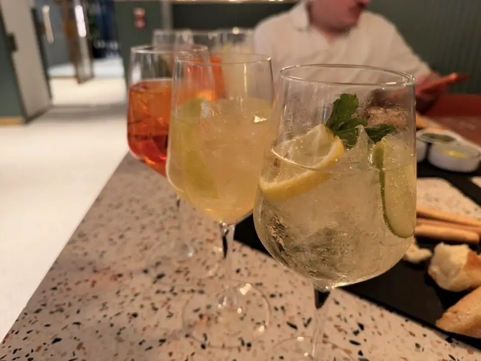 Three cocktails with ice and citrus garnishes on a speckled countertop, blurred person in white in background