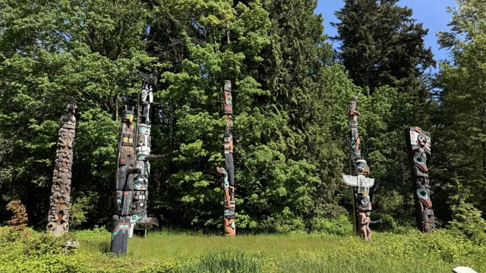 Tall carved totem poles stand in a grassy clearing with trees