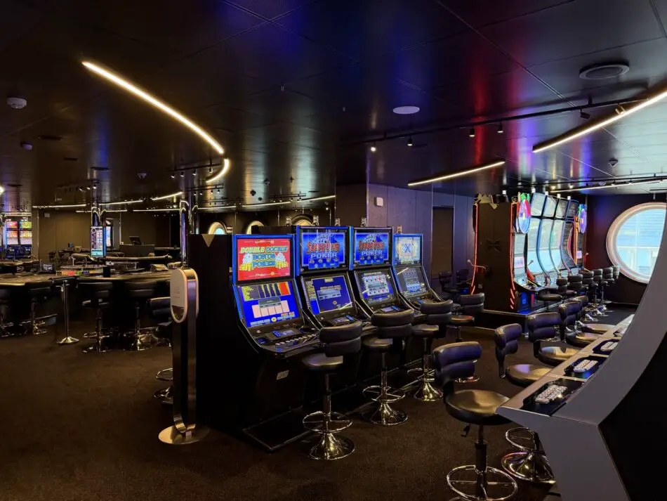 Inside a cruise ship casino with rows of slot machines and stools