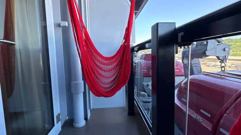 Virgin Voyages cruise ship balcony with a red hammock and glass railing, offering an ocean view.