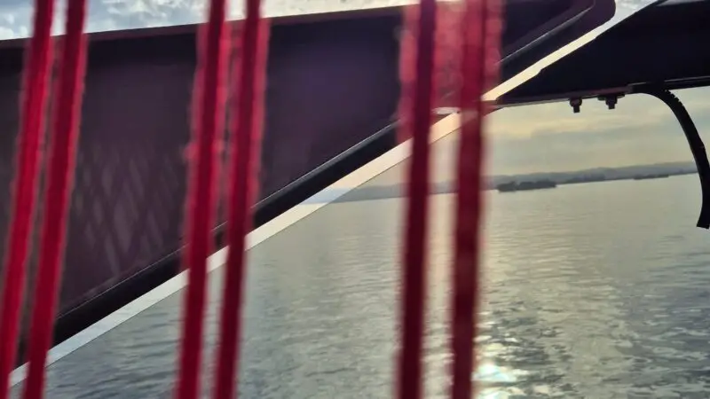 View from a Virgin Voyages cruise ship balcony, showing red ropes and the ocean with a cloudy sky and sun in the background.