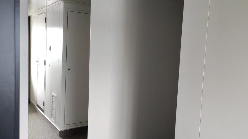 Virgin Voyages cruise ship cabin hallway with white walls, a large mirror, and gray carpet.