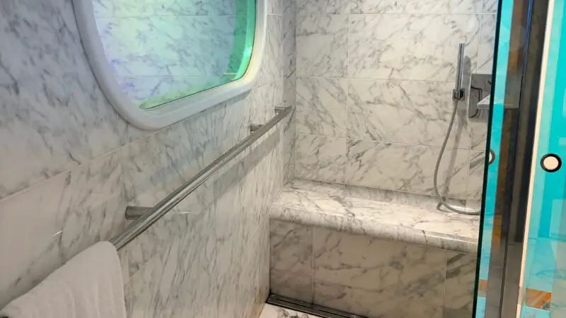 Cruise ship cabin bathroom with marble decor, a round shower head, a glass shower door, and a towel hanging on a rail.