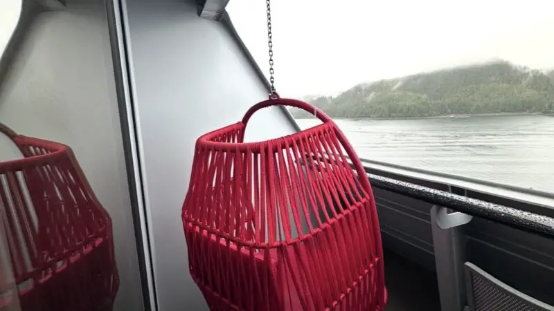 Virgin Voyages cruise ship balcony with a red hanging chair, small table, and outdoor view.