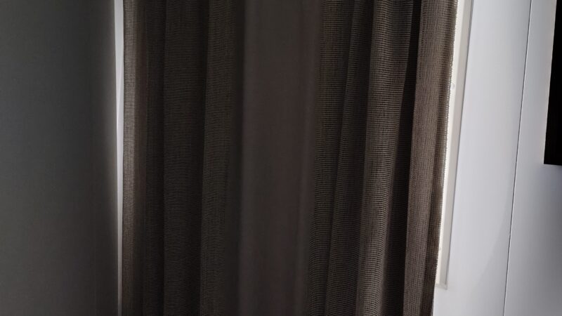A Virgin Voyages cruise ship cabin with closed brown curtains and subtle lighting.