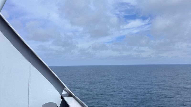 View from a Virgin Voyages cruise ship balcony overlooking the ocean with a cloudy sky.