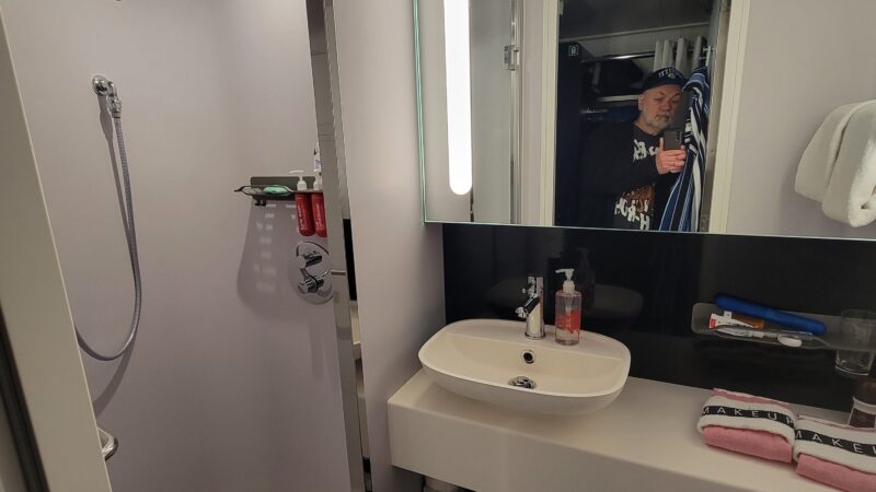 Virgin Voyages cruise ship cabin bathroom with a shower, sink, mirror, and toiletries.