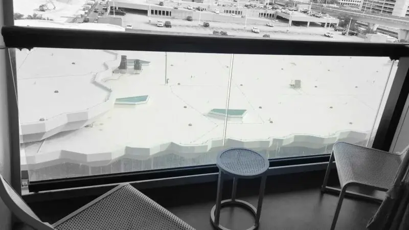 Virgin Voyages cruise ship balcony cabin with two metal chairs and a small round table overlooking a rooftop view.