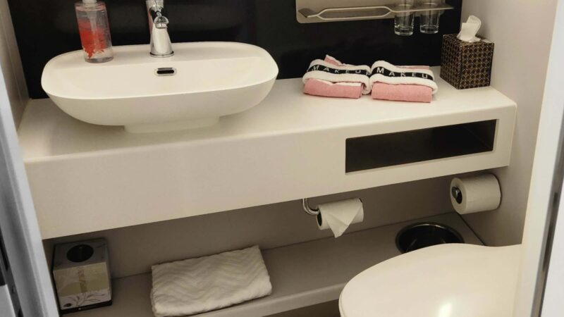 Bathroom in a Virgin Voyages cruise ship cabin with a white sink, soap dispenser, towels, and toiletries on the vanity.