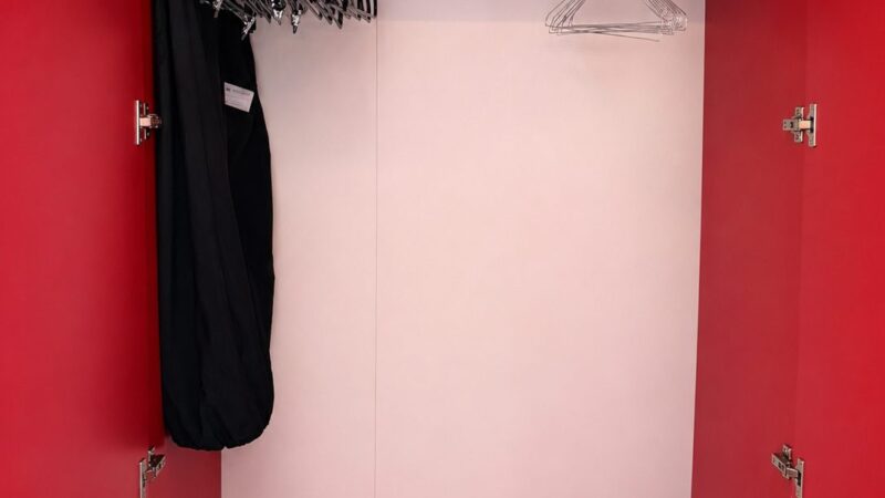 Red closet in a Virgin Voyages cruise ship cabin, with hangers, a garment bag, and red storage bags on the shelf.