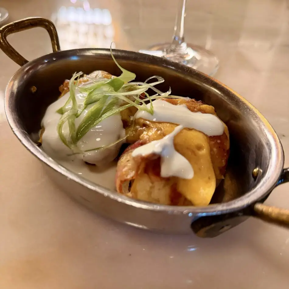 Small skillet of crispy potatoes topped with white sauce and scallions on a Virgin Voyages cruise ship