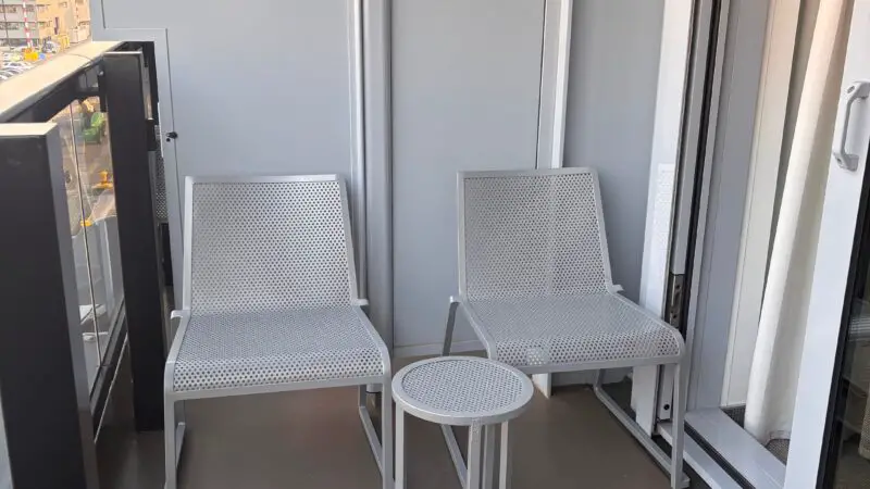 Balcony of a Virgin Voyages cruise ship cabin featuring two white perforated chairs and a small round table.