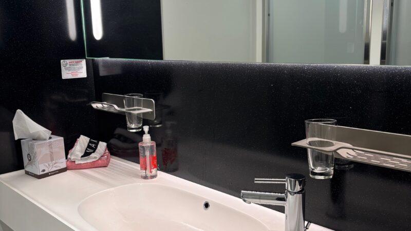 Bathroom in a Virgin Voyages cruise ship cabin, featuring a white sink, chrome faucet, and mirror, with toiletries on the counter.