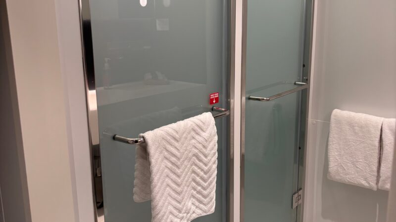 Cruise ship cabin bathroom with frosted glass shower doors and white towels on towel bars.