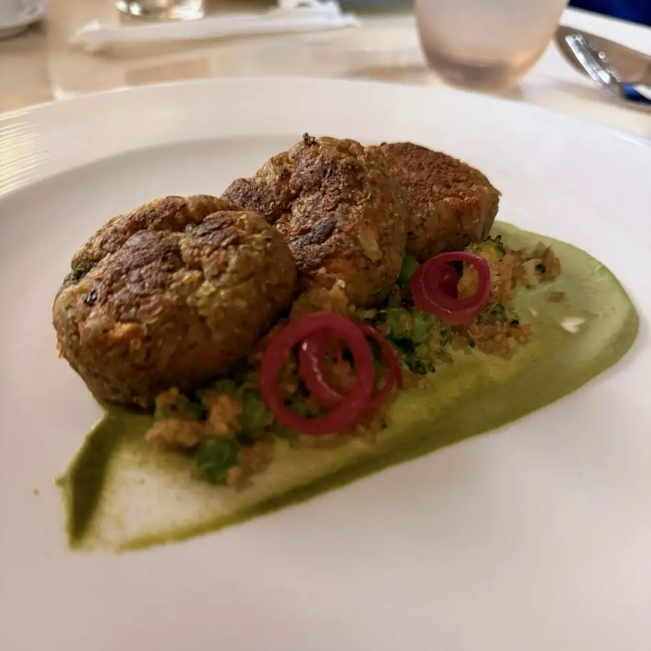 Two fried croquettes served on green sauce with vegetables and red onion rings
