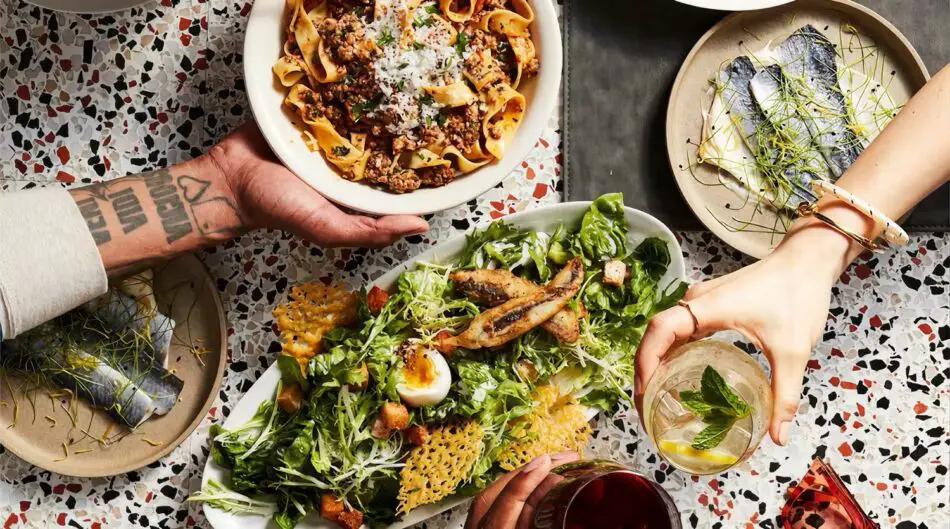 Top-down view of a shared meal with pasta, salad, and grilled fish plates