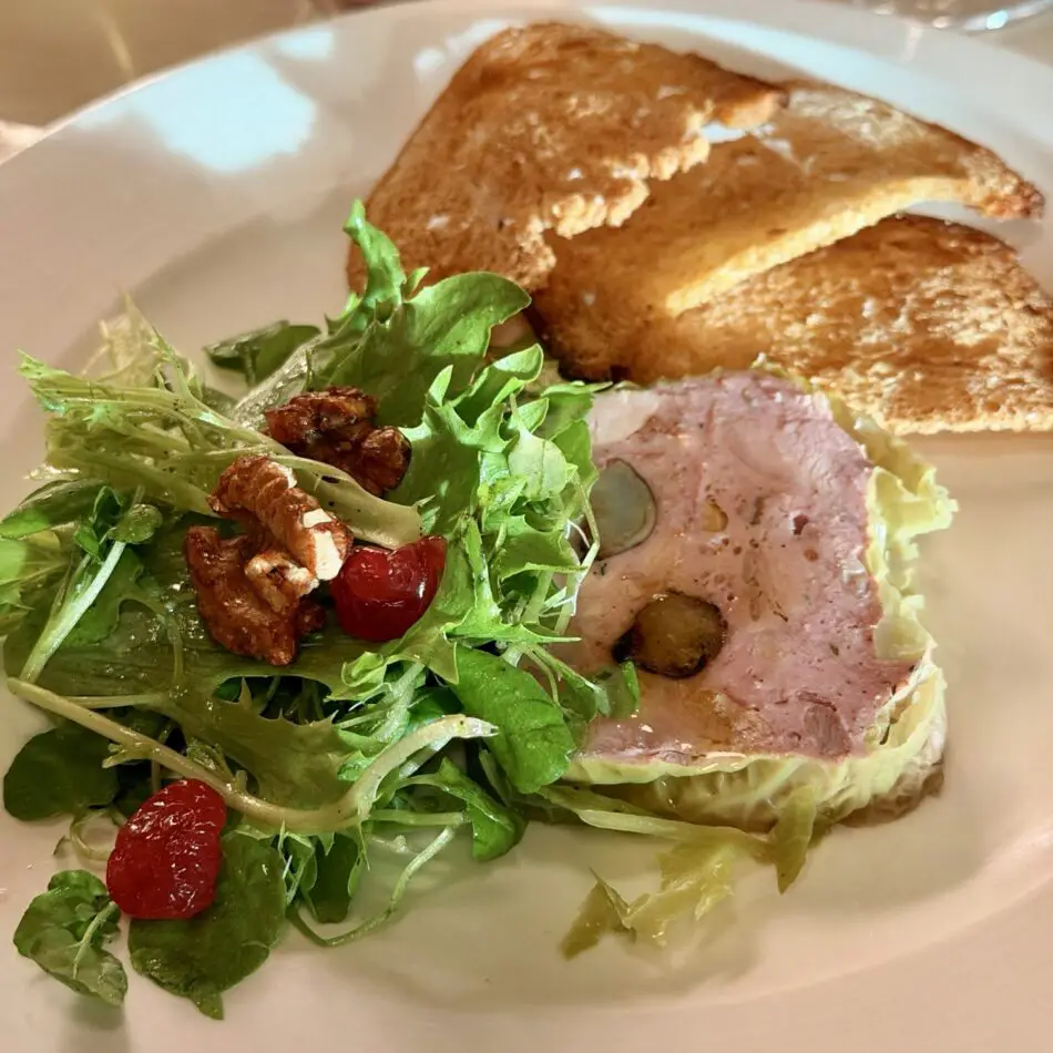 Plate of green salad with walnuts and cranberries, plus sliced meat roulade and toasted bread