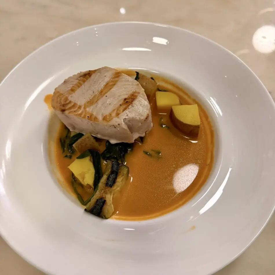 Seared white fish fillet in orange sauce with potatoes and greens