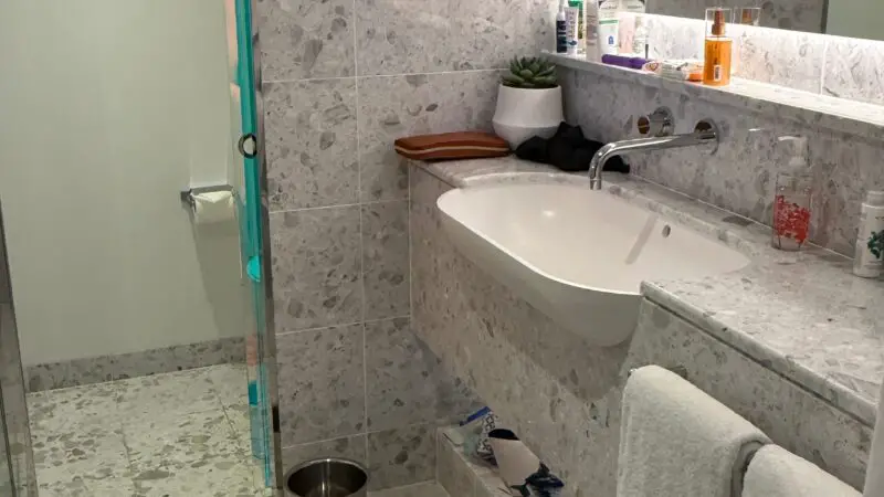 Spacious bathroom in a Virgin Voyages cruise ship cabin with a modern sink, mirror, toiletries, and tile flooring.