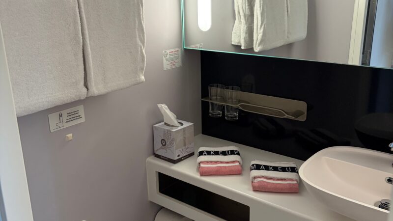 Virgin Voyages cruise ship cabin bathroom with a modern sink, toilet, towels, and a large mirror.