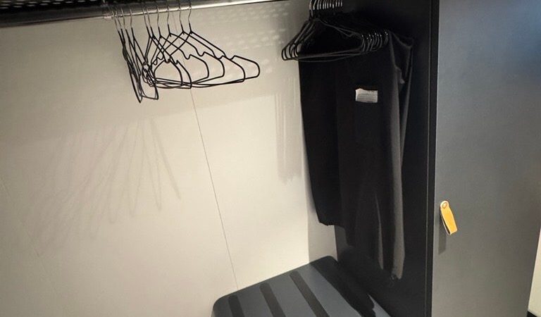 Open wardrobe in a Virgin Voyages cruise ship cabin with hangers, a shelf, and a storage unit.