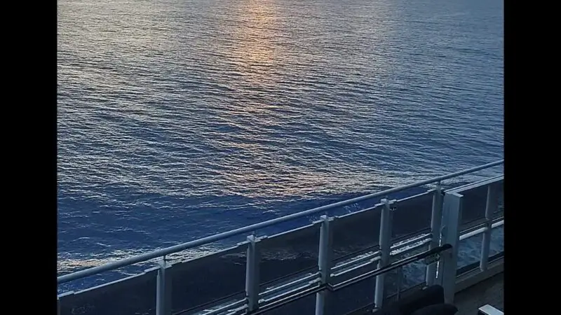 View from a Virgin Voyages cruise ship cabin balcony, showing the ocean and a cloudy sunset.