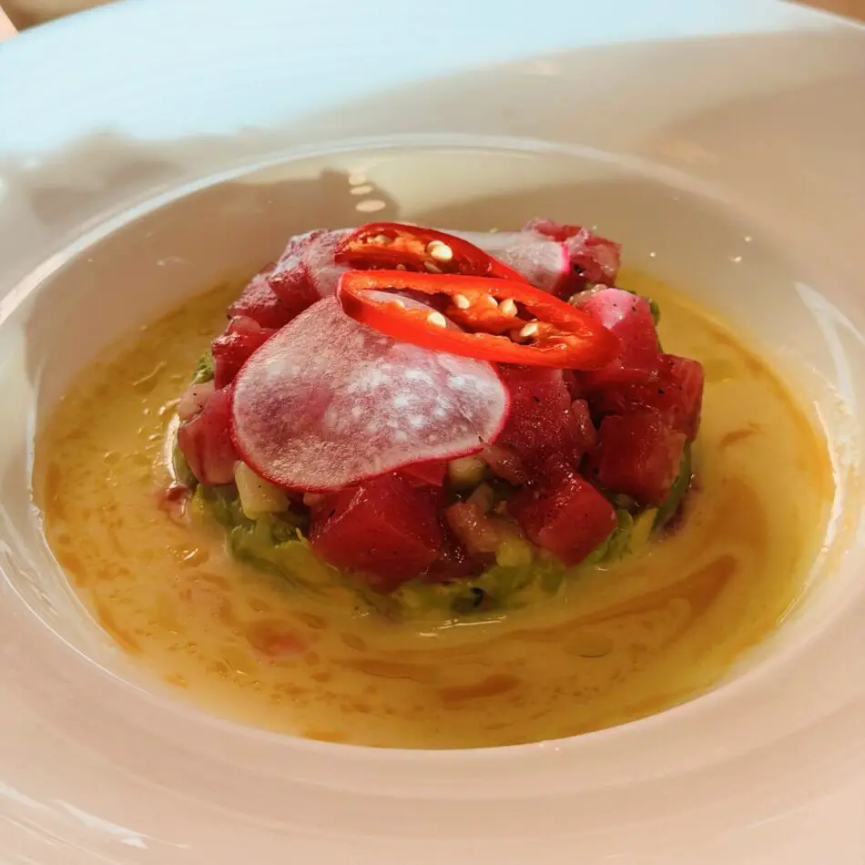 Tuna tartare topped with red chili slices in a yellow sauce