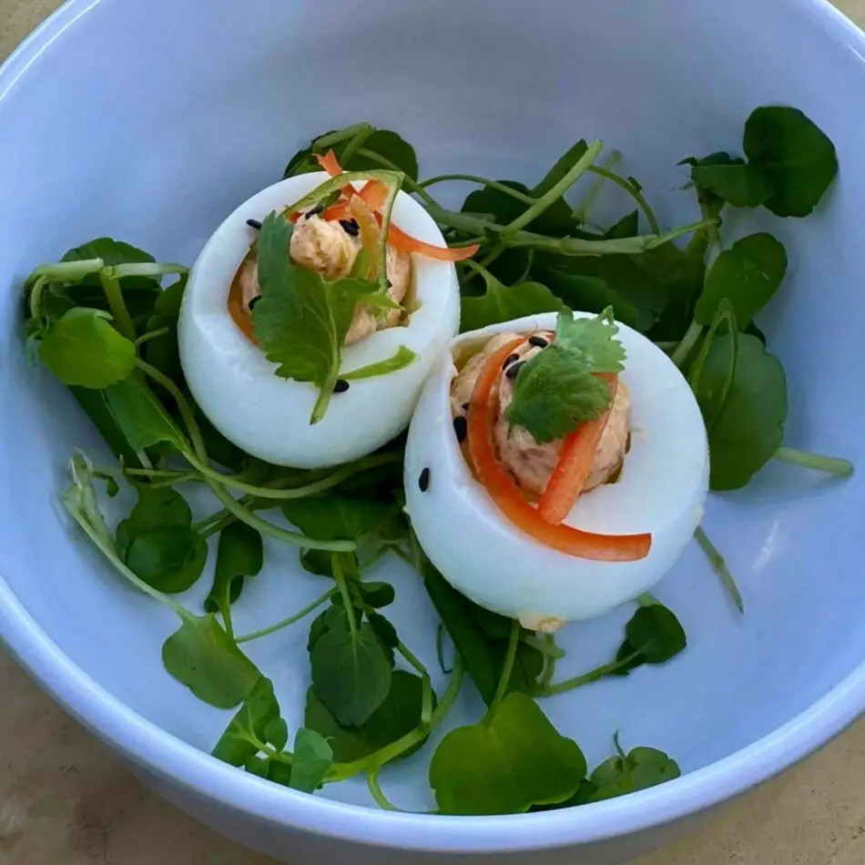Two stuffed hard-boiled eggs with carrot ribbons and cilantro in a blue bowl