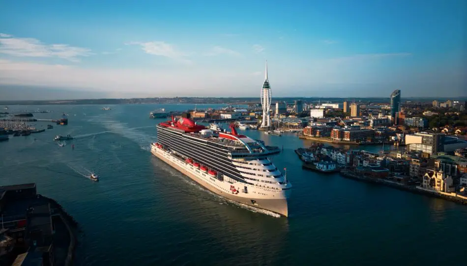 Virgin Voyages cruise ship sailing past a coastal city skyline